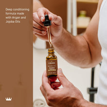 Beard oil dropper dispensing oil above Cremo Bourbon Vanilla bottle