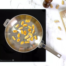 Stainless steel steamer pan on stovetop holding small pieces of food