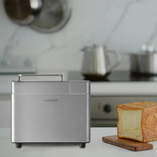 Stainless steel bread maker on countertop with loaf of bread beside it
