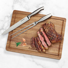 Stainless steel carving knife and fork on wood board with meat slices