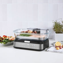 Digital glass steamer with clear lid on countertop, steaming assorted food in basket