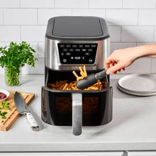 Air fryer with open basket as food is added, stainless body and front pull handle