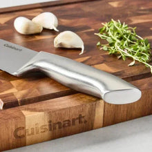 Stainless steel chef knife on wooden cutting board with sliced onions and herbs
