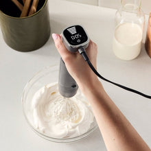 Hand holding immersion blender blending in a glass cup with whisk attachment