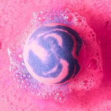 Bath bomb dissolving in water, round fizz ball with pink foam and purple-blue swirls