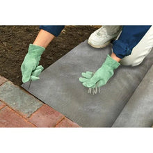 Gray landscaping fabric sheet laid flat on ground with gloves and pavers nearby