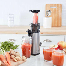 Compact cold press power juicer with orange juice cups and fresh produce beside it.
