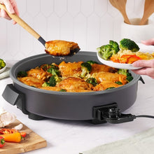Gray electric skillet with side handles and open lid, topped with saucy chicken and broccoli