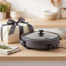 Gray electric ceramic skillet on wood counter with lid and power cord attachment