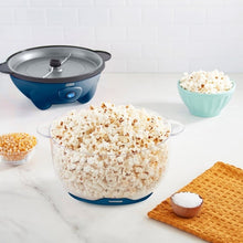 Blue ceramic popcorn maker on counter with clear lid; bowls of popcorn nearby