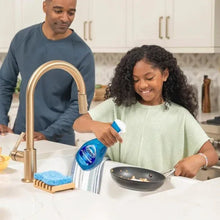 Dish soap spray bottle held above pan with a second blue bottle nearby