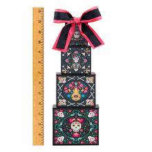 Four-tier candy treat tower with black patterned boxes and red-black bow, beside ruler