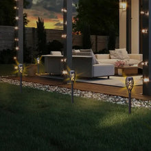 Set of lit solar tiki torch lights on a lawn near outdoor seating and a patio