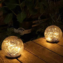 Two warm glowing gold crackle glass LED globe solar lights with black stake bases on wood deck