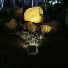 Solar rock landscape light in rocky garden bed, circular lens glowing warmly at night