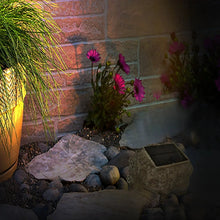 Solar rock light beside flower bed at dusk, stone housing with warm glow