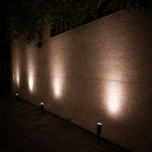 Solar spotlights projecting bright warm white illumination along a garden wall at night