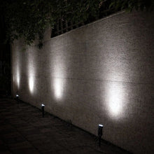 Solar spotlights projecting bright white light along a garden wall and path at night