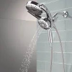 Chrome hand shower head spraying water from wall-mounted shower system