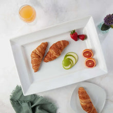 White rectangular stoneware platter with raised rim, with croissants and fruit