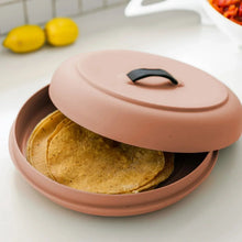 Tortilla warmer lid in terra-cotta with black handle, covering a tortilla