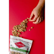 Shelled walnut kernels spilling on a red surface with a hand holding pieces.
