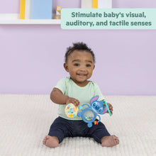 Baby holding blue Stitch tummy tumble activity toy with round mirror and dangling pieces