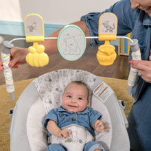 Baby in gray Pooh-print bouncer with spinning toy bar holding character pieces