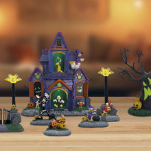 Halloween village decoration with a purple haunted house and small characters on gray stone bases