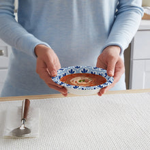 Hand holding a printed 12 oz paper bowl with blue leaf pattern and food inside
