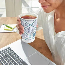 Insulated paper cup with teal geometric design, held in hand with hot drink