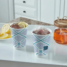 Insulated paper cups with teal geometric pattern, filled with beverages on table