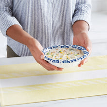 Hands holding a blue patterned paper bowl on a table, empty and ready