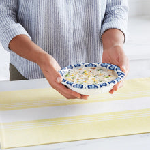 Paper bowl with blue leaf pattern rim, held by hands over a table