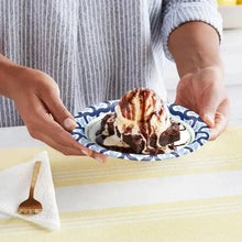 Paper plate with blue leaf pattern and grilled food, held by hands.
