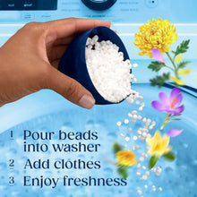 Hand holding cup pouring white scent booster beads into a washing machine.