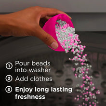 Laundry scent booster beads pour from a pink scoop into a washer