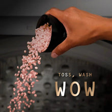 Pink laundry scent booster beads pouring into washer drum