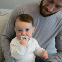 Baby seated wearing a light outfit with a white pacifier
