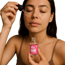 Facial oil in dropper bottle held to a woman’s cheek with eyes closed.