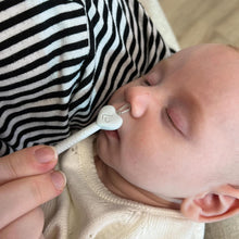 Baby with nasal aspirator nozzle near nose, white device with green indicator button