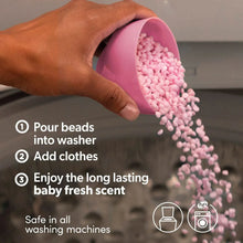 Hand pouring pink scent booster beads from a bottle into a washer