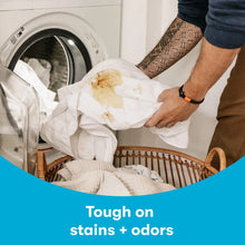Laundry being handled near washer with 'Tough on stains + odors' message