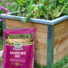 Organic raised bed mix bag next to wooden raised bed with green plants.