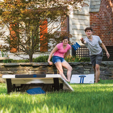 Outdoor cornhole set with white board, blue stripe, and bean bags on tabletop