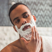 Shaving gel lather on a man's cheek, hand spreading foam