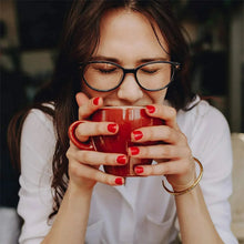 Person holding and drinking from a red coffee mug