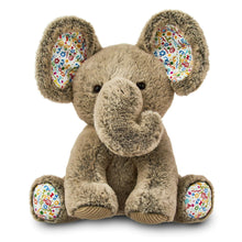 Gray plush elephant toy with colorful belly patch, sitting with floppy ears and trunk.