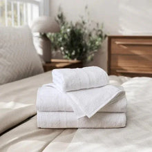 White bath towels folded, with one towel draped over the stack on a bed.