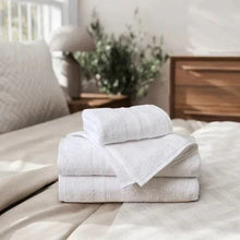 White bath towels folded into a neat stack on a bed